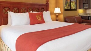 Ein Hotelzimmer mit einem großen Bett, einem Holzkopfschild, einer roten Tagesdecke und einem Schreibtisch mit einer Lampe.