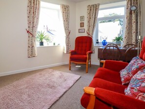 A living room with a red armchair, a sofa, a dining table with chairs, and a window with curtains. - Chyancrowse (Penzance)