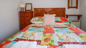A bedroom with a wooden headboard, a bed with a colorful quilt, a wooden dresser, a bedside table with a lamp, and a mirror on the wall. - Chyancrowse (Penzance)
