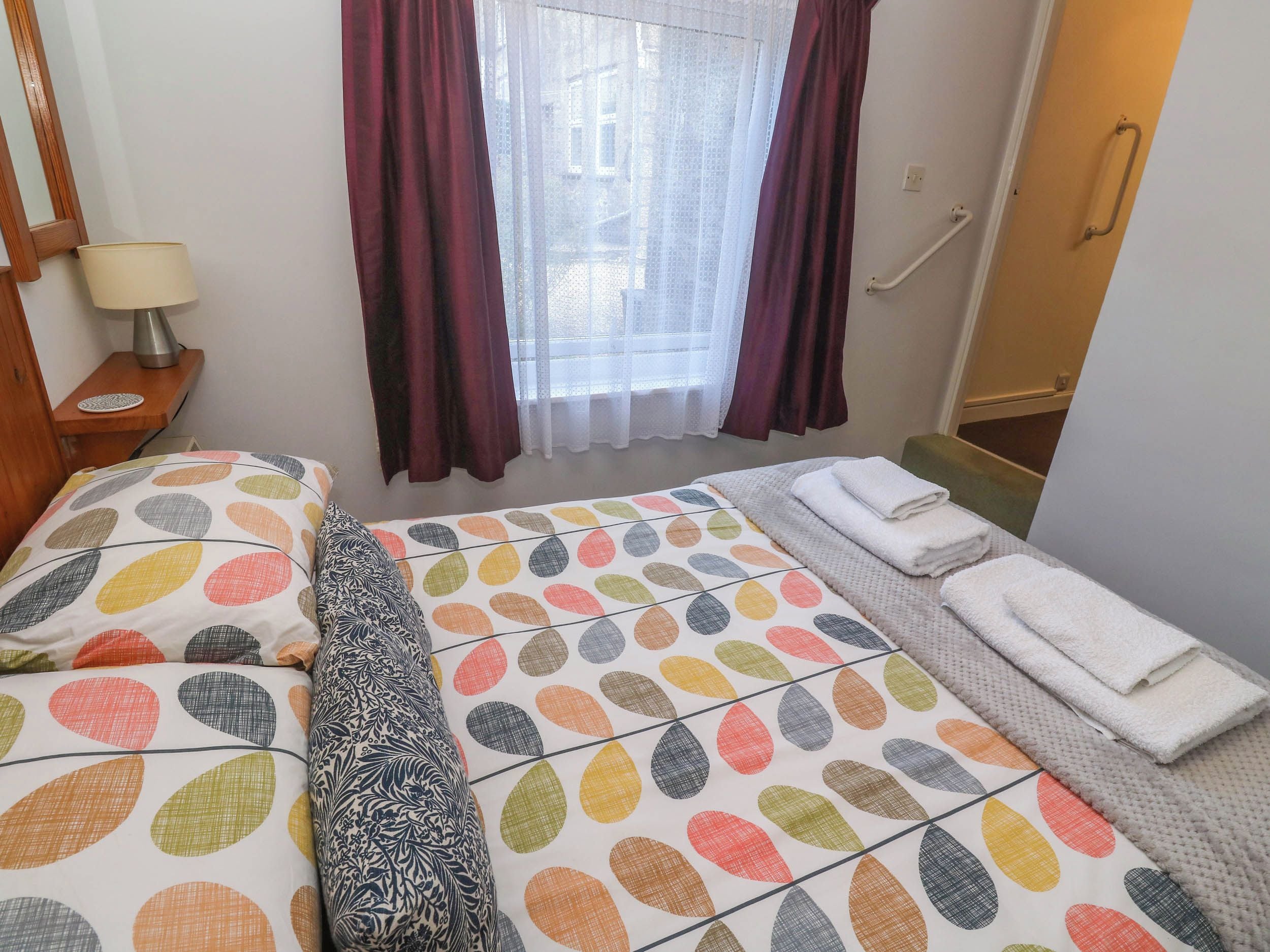 Habitación de hotel con cama, mesita de noche con lámpara, ventana con cortinas y puerta de baño.