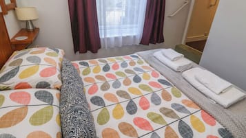 Habitación de hotel con cama, mesita de noche con lámpara, ventana con cortinas y puerta de baño.