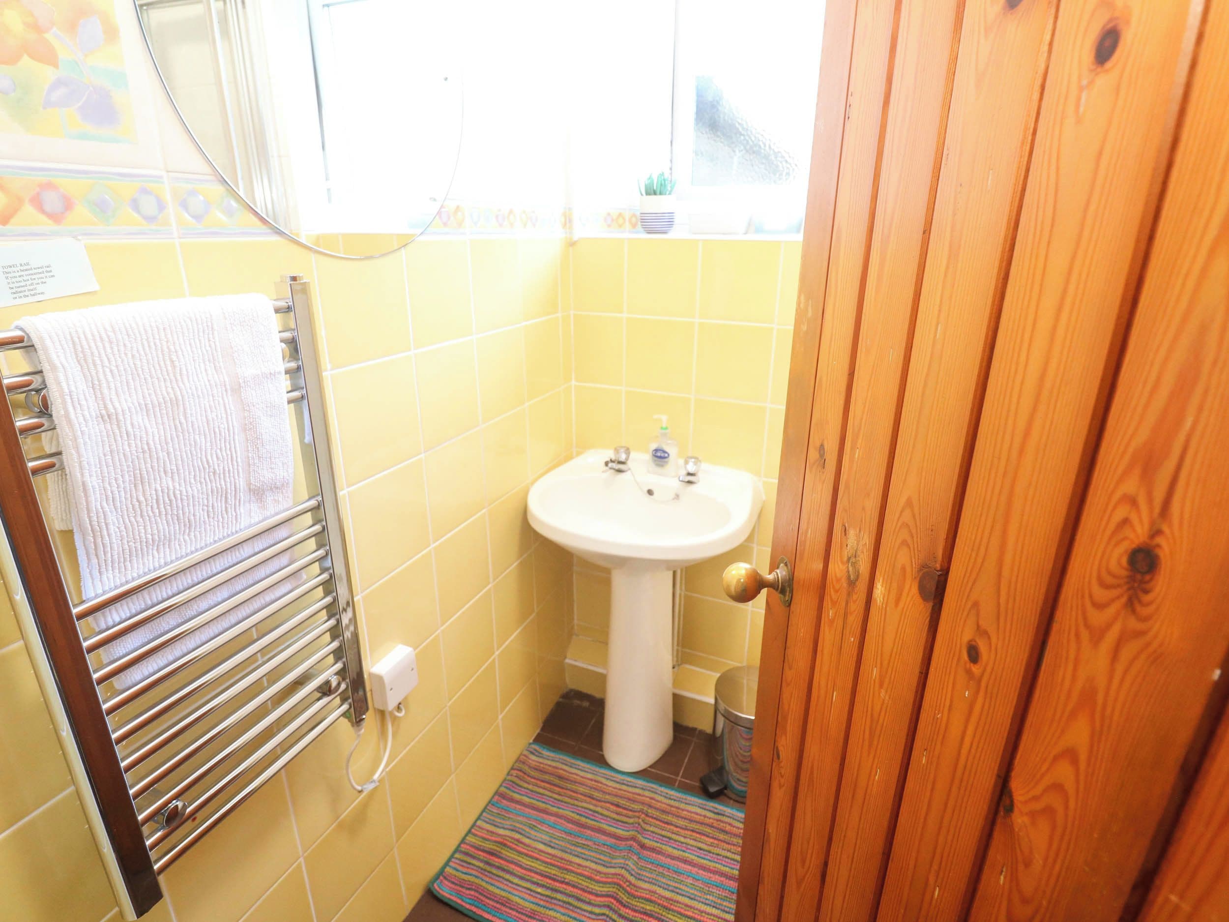 Une salle de bain avec des carreaux jaunes, un lavabo blanc, un porte-serviettes et une porte en bois.