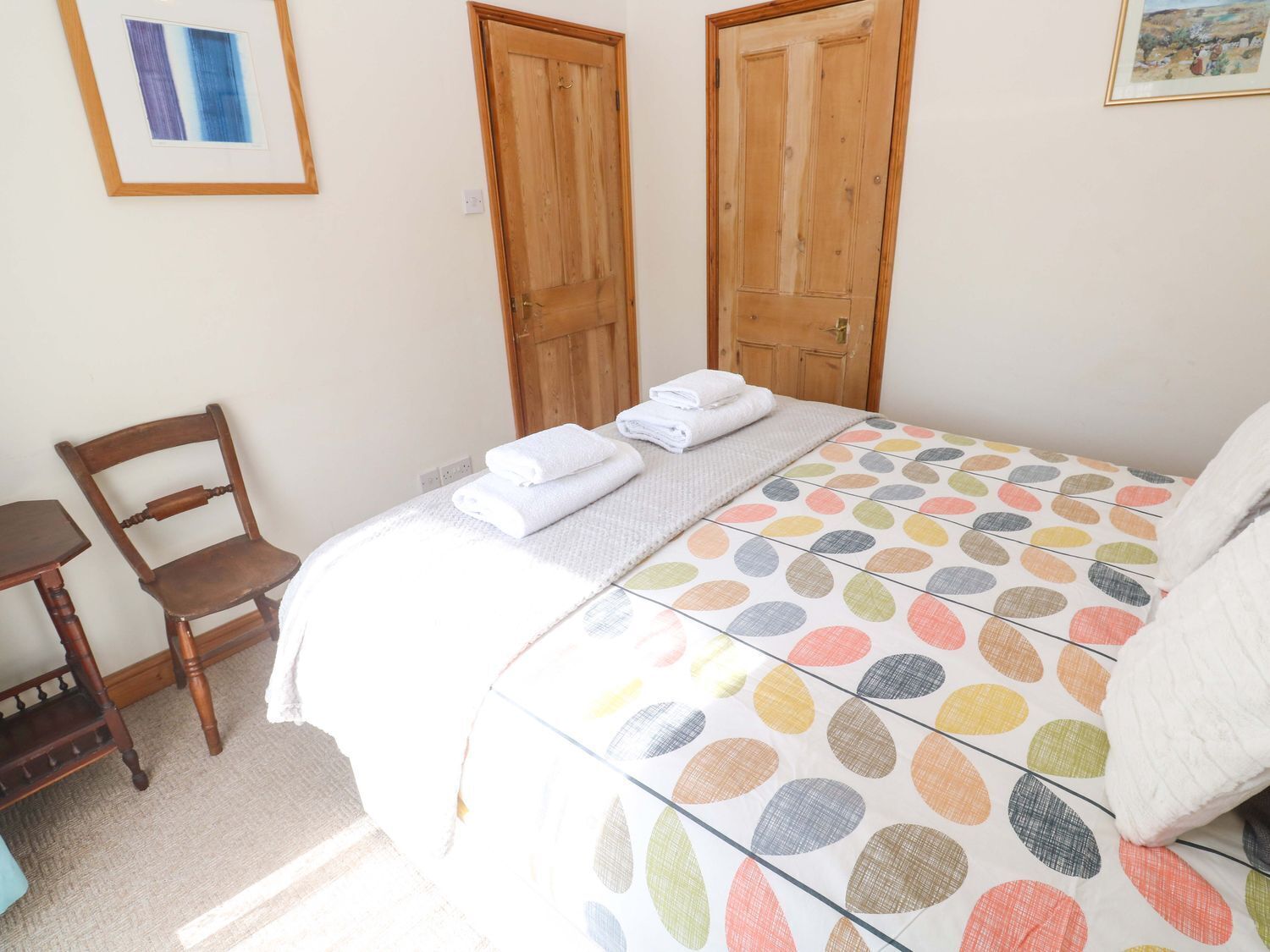 Un dormitorio con cama, una silla, dos puertas de madera y un cuadro en la pared.