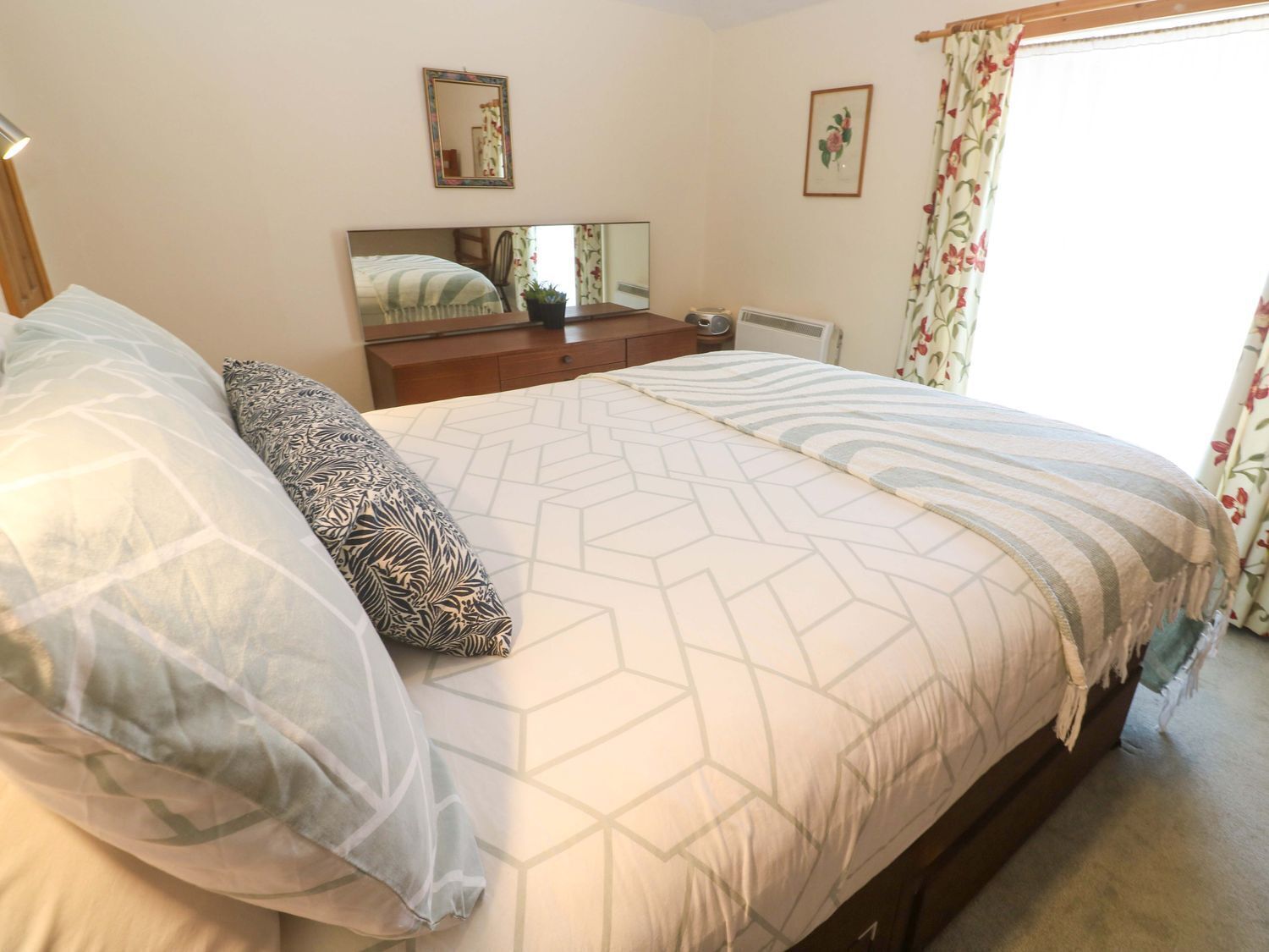 A bedroom with a bed, a dresser, a mirror, and a window with curtains.