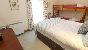 Un dormitorio con literas, un escritorio, una silla, un radiador y una ventana con cortinas florales.
