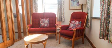 A room with two red armchairs, a small wooden table, a lamp, and a framed picture on the wall.