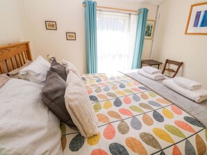 A bedroom with a bed, pillows, a bedside table, a chair, and a window with curtains. - Chyandaunce (Penzance)