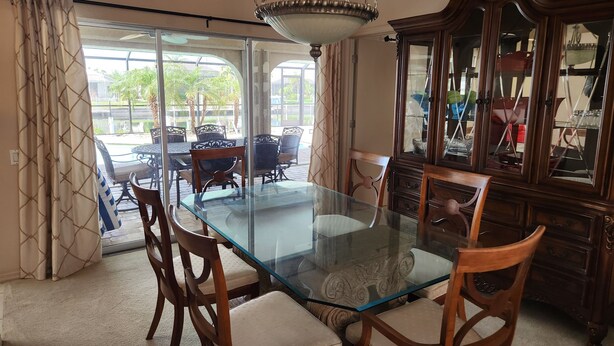 A dining area with a glass table, wooden chairs, a chandelier, and a view through a glass door to an outdoor patio. - Sailboat waterfront home with 60 ft dock on deep canal and heated pool (Punta Gorda)