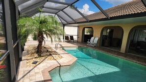 An indoor swimming pool with a tiled floor, a palm tree, and lounge chairs. - Sailboat waterfront home with 60 ft dock on deep canal and heated pool (Punta Gorda)