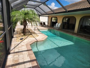 An indoor swimming pool with a tiled floor, a palm tree, and lounge chairs. - Sailboat waterfront home with 60 ft dock on deep canal and heated pool (Punta Gorda)