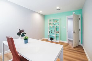 Une pièce avec une table blanche, une chaise rouge, un mur de couleur turquoise et une porte blanche.