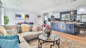 A modern living room with a sofa, coffee table, and a view into the kitchen. - The Escape Insurance approved Single story Pool (Los Angeles)