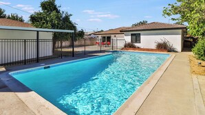 A rectangular swimming pool with a tiled edge, surrounded by a concrete deck and a metal fence. - The Escape Insurance approved Single story Pool (Los Angeles)