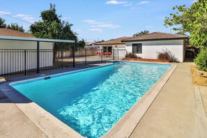 Une piscine rectangulaire dont le bord est recouvert de carreaux, entourée d’une terrasse en béton et d’une clôture en métal.