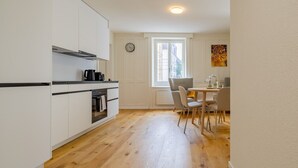 Una cuina compacta amb armaris blancs, un forn de sobre i una màquina de cafè.