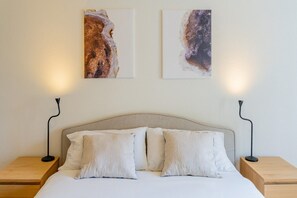 Ein Schlafzimmer mit einem Bett, zwei Nachttischen, zwei Wandlampen und zwei abstrakten Bildern.