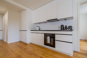 Cuina moderna amb armaris blancs, tauleig negre i forn integrat.