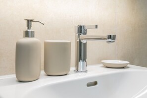 Ein Waschbecken mit chromfarbenem Wasserhahn, einer Seifenspender und einer Schale.