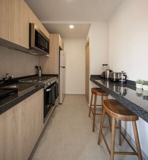 A modern kitchen with wooden cabinets, a stainless steel range, a built-in microwave, and a coffee maker. - Refined Spacious Studio, Balcony, Pool & Gym (Mexico City)