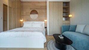 Et soveværelse med seng, sengeborde, et rundt sofabord, en sofa, et garderobeskab og en vægmonteret lampe.