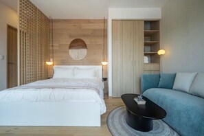 A bedroom with a bed, bedside tables, a round coffee table, a sofa, a wardrobe, and a wall-mounted light fixture. - Refined Spacious Studio, Balcony, Pool & Gym (Mexico City)