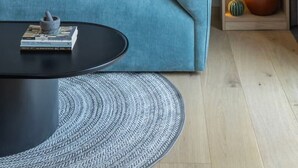 En moderne stue med en blå sofa, et sort sofabord og en træbogreol med dekorative genstande.