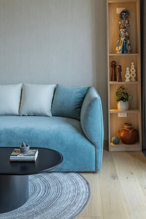 Un salon moderne avec un canapé bleu, une table basse noire et une bibliothèque en bois agrémentée d’objets décoratifs.