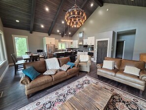 A spacious living area with leather sofas, a dining table, and a kitchen in the background. - 4-bedroom Mountain home above the Vallecito Reservoir with AC, fitness room (Bayfield)
