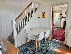A dining area with a white table and chairs, a wooden staircase, and a red patterned rug. - Penpegws (Aberystwyth)