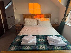 Un dormitorio con cabecera de madera, ropa de cama blanca, dos lámparas de noche y una ventana con vistas.