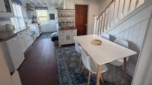 Una cocina con armarios blancos, una mesa de comedor y una escalera.