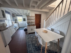 A kitchen with white cabinets, a dining table, and a staircase. - Penpegws (Aberystwyth)