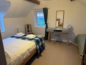 Un dormitorio con cama, escritorio, silla, espejo y ventana con cortinas.