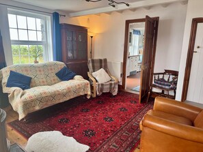 A living room with a patterned sofa, a wooden chair, a red carpet, and a view through an open door. - Penpegws (Aberystwyth)