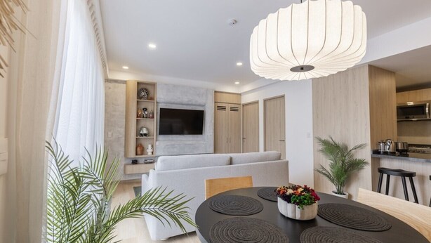 Un salon moderne comprenant un canapé, une table à manger avec des sets de table, un luminaire suspendu et un coin cuisine équipé d’un four à micro-ondes.