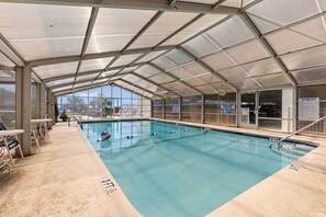 Ein Hallenbad mit klarem Wasser, einem Sprungbrett und einem überdachten Bereich mit Sitzgelegenheiten.