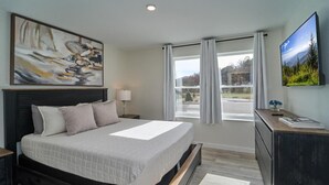 Ein Schlafzimmer mit Bett, Fernseher, Schreibtisch, einem Fenster mit Vorhängen und Bildern an den Wänden.