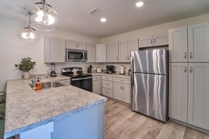 A modern kitchen with granite countertops, stainless steel appliances, and light-colored cabinetry. - The Ruby 100 (Pigeon Forge)