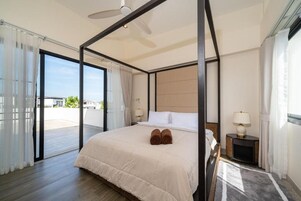 A four-poster bed with a headboard, a bedside table with a lamp, and a view through a glass door to an outdoor area.