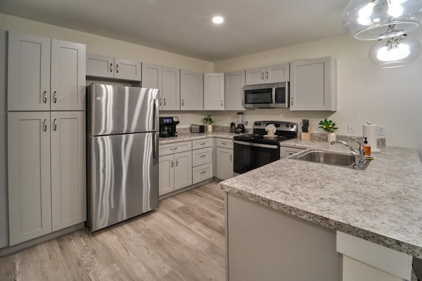 Una cocina moderna con electrodomésticos de acero inoxidable, encimeras de granito y armarios color gris claro.