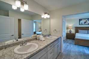 A bathroom with two sinks, a large mirror, and a wooden bed in the adjacent room. - The Ruby 101 (Pigeon Forge)