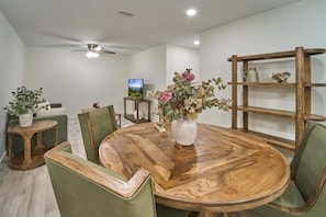 A dining area with a round wooden table, green upholstered chairs, a wooden shelf unit, and a television on a stand. - The Ruby 101 (Pigeon Forge)