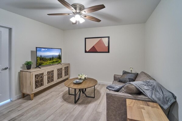 Ein Wohnzimmer mit Fernseher, Deckenventilator, Schrank, Sofa und Couchtisch.