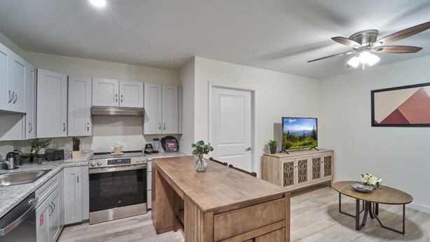 A modern kitchen with white cabinets, a wooden island, a built-in oven, and a ceiling fan. - The Ruby 102 (Pigeon Forge)