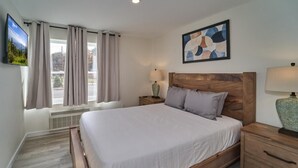 A bedroom with a bed, nightstands, a TV, a window with curtains, and a painting on the wall. - The Ruby 102 (Pigeon Forge)