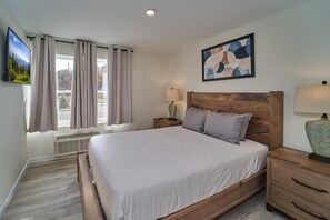 Ein Schlafzimmer mit Bett, Nachttischen, einem Fernseher, einem Fenster mit Vorhängen und einem Bild an der Wand.