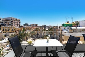 Un balcón con mesa y sillas, con vistas a un paisaje urbano con edificios y palmeras.