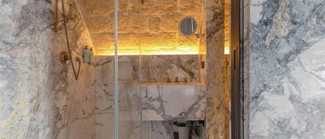 A bathroom with a marble wall, a glass shower enclosure, and a sink with a mirror above it.