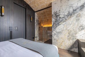 Ett modernt hotellrum med en stor säng, väggar i marmor och en duschkabin med glasväggar.