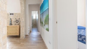Un pasillo con pared de piedra, cómoda de madera y cama con colcha azul.